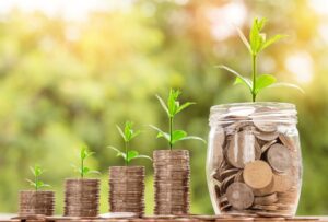 stacks of coins progressively grow taller from left to right, ending with a jar of coins. Each stack has a small plant that grows larger with each stack, symbolizing growth in revenue.